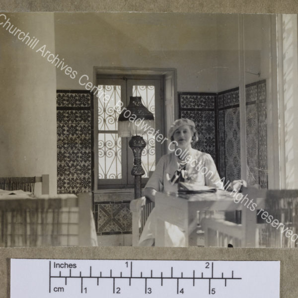 Photograph of CSC [while on a cruise of the Eastern Mediterranean on 1st Lord Moyne's yacht the Rosaura].  She is sitting at a table in a [?] cafe with tiled walls