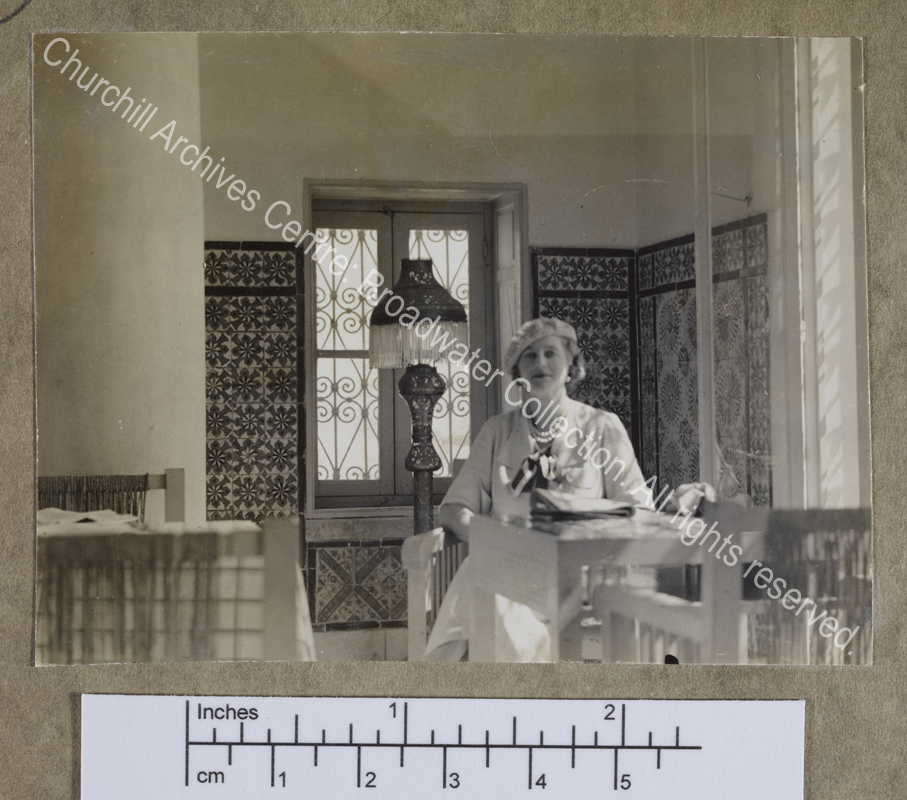 Photograph of CSC [while on a cruise of the Eastern Mediterranean on 1st Lord Moyne's yacht the Rosaura].  She is sitting at a table in a [?] cafe with tiled walls